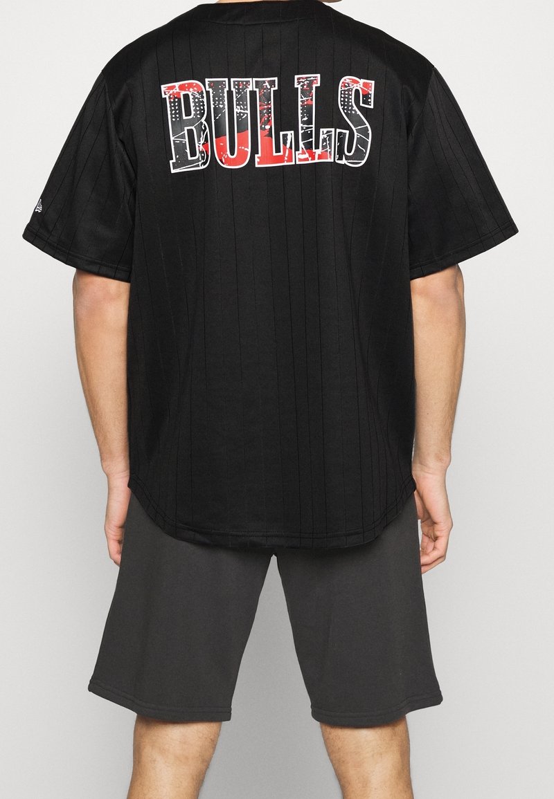 Jersey negro de manga corta con rayas verticales y "Bulls" en letras bold blancas y rojas en la parte posterior. Combinado con pantalones cortos grises.