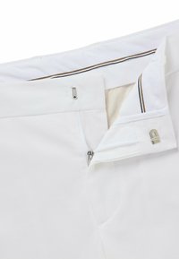 White pants featuring a zipper and button closure. Interior has contrasting tan lining with a narrow brown stripe along the waistband.