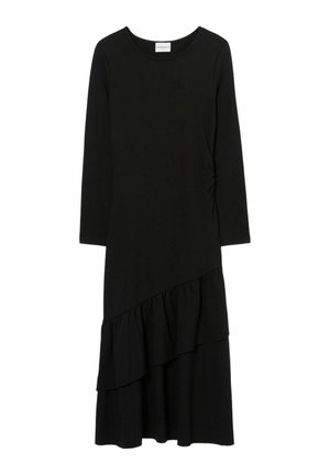 Mujer con vestido midi negro de manga larga con detalle de volantes, pañuelo azul con estampados, tacones negros con tiras y bolso marrón.