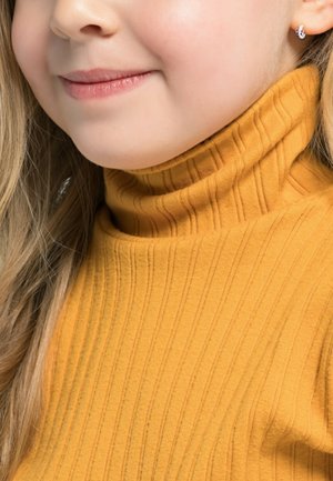 Maglione a collo alto a coste giallo senape, con un collo alto, caratterizzato da linee verticali e una texture morbida, indossato da una persona con capelli biondi mossi.