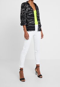 Maglietta nera con motivo a disegno bianco, top verde neon, pantaloni bianchi aderenti e tacchi alti neri con cinturini.