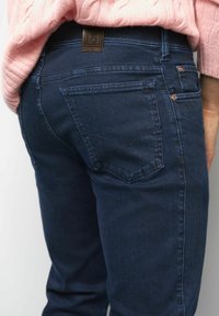 Persoon in donkerblauwe denim jeans en een roze gebreide trui, weergegeven van de achterkant en tot aan de taille.