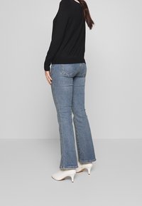 Svart långärmad tröja i kombination med ljusblå utställda jeans och vita högklackade skor. Jeansens har bakfickor och en subtil avblekning.