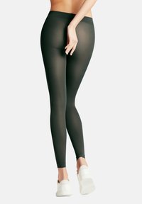 Leggings neri elasticizzati con vita alta, texture morbida e design a tutta lunghezza, abbinati a scarpe da ginnastica bianche.