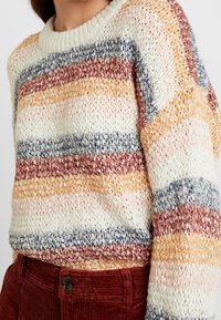 Suéter de punto con rayas horizontales en crema, naranja, azul y rojo. Tejido texturizado con cuello redondo y corte holgado.