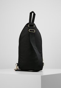 Borsa a tracolla in tessuto nero con una forma elegante e allungata. Spallaccio regolabile resistente e hardware in tonalità oro. Texture liscia, design minimalista.