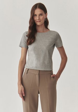 Camiseta corta de manga corta en gris, de una tela suave, con cuello redondo y una silueta ajustada, combinada con pantalones beige de tiro alto.