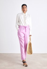 Chemise blanche à col, pantalons rose avec cordon de serrage, sandales avec accents noirs et crème, et un sac fourre-tout tissé beige. Tissu lisse et léger.