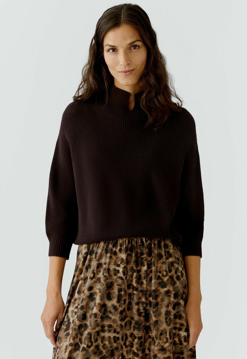 Bruine gebreide trui met een hoge hals en driekwartmouwen, gecombineerd met een rok met luipaardprint en een gathered taille.