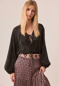 Blusa negra con mangas abullonadas y un detalle de lazo en el cuello, combinada con una falda rosa con estampado floral y un dobladillo con volantes.