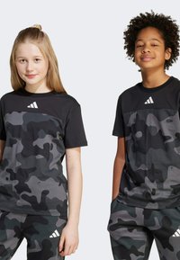Black and gray camouflage t-shirts with round necks and short sleeves. Features Adidas logo on the upper front. Coordinating pants visible.