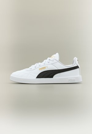 Baskets Puma blanches avec une bande noire, logo Puma doré, semelle texturée et lacets blancs, présentées en profil latéral sur un fond neutre.