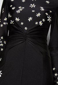 Black dress with long sleeves, featuring white and yellow daisy embroidery. Ruched detail at the waist, smooth fabric texture.
