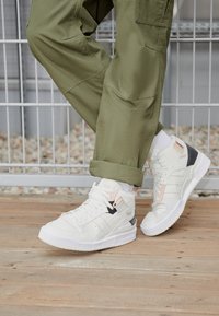 Höga sneakers i vitt läder med svarta, rosa och grå accenter. Strävt yta, tjock vit sula, med tre ränder och logotyp.