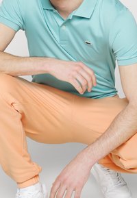 Ein hellblaues Polohemd mit einem kleinen Logo, kombiniert mit orangen Jogginghosen. Das Outfit bietet eine lockere Passform und einen weichen Baumwollstoff.