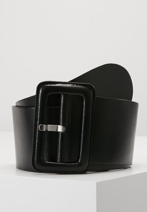 Ceinture large en cuir noir avec grosse boucle rectangulaire rembourrée et ardillon en argent, présentée enroulée sur une surface blanche.