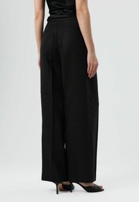 Zwarte broek met wijde pijpen van een gestructureerde stof, met een hoge taille en achterzakken, gecombineerd met zwarte open-toe hakken.