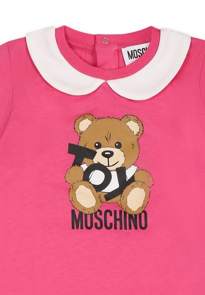 Camicia in cotone rosa con una grafica di un orsetto che tiene un cartello nero con la scritta "TOY", colletto bianco e testo nero "MOSCHINO".