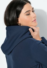 Sudadera azul marino con una textura suave, con una capucha gruesa y detalles de costura prominentes, sostenida por el cuello.