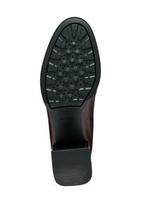 Zapato de cuero marrón con suela de goma negra texturizada que presenta patrones de agarre prominentes y un tacón ligeramente elevado. Logotipo de la marca visible.