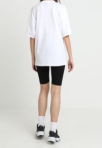 Una camiseta blanca de gran tamaño con mangas cortas, combinada con unos pantalones cortos de ciclista negros ajustados. Se llevan zapatillas deportivas negras y calcetines blancos.