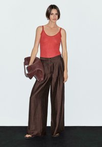 Red ribbed tank top, brown wide-leg pants, and textured brown handbag. Smooth fabric with subtle sheen. Minimal accessories.