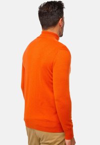 Pull à col roulé orange avec des poignets et un bas côtelés, fabriqué dans un matériau doux, présentant un design ajusté et une texture lisse.
