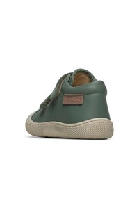 Chaussure en cuir vert avec une semelle en caoutchouc texturée, dotée d'un patch logo beige et de lacets. Le design est bas et arrondi au niveau des orteils.