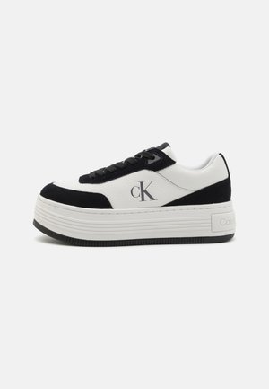 Białe i czarne sneakersy na platformie z materiałów zamszowych i skórzanych, z wyraźnym logo, teksturowaną powierzchnią oraz sznurowanym designem.