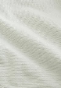 Tissu blanc avec un motif texturé en damier semblable à une alvéole et des plis subtils créant de douces ombres.