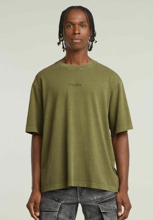 T-shirt oversize verde oliva in cotone, con scollo a giro e discreto dettaglio logo frontale. Maniche corte e taglio rilassato.