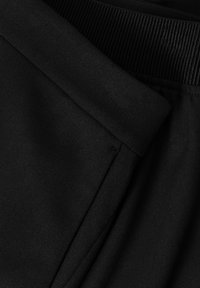 Black fabric, smooth texture, visible waistband with ribbed design. Features a seam and pocket opening. Close-up view highlights details.