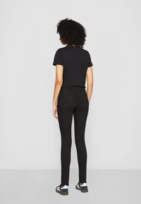 T-shirt en coton noir à manches courtes porté avec un jean skinny noir. La tenue présente un design minimaliste, complété par des baskets sombres.