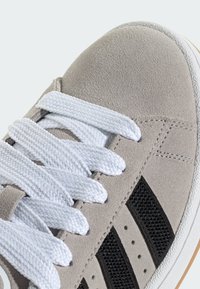 Grauer Wildleder-Sneaker mit weißen Schnürsenkeln, schwarzen Mesh-Streifen und einer strukturierten Zehenkappe. Gummisohle mit kontrastierendem Randdetail.
