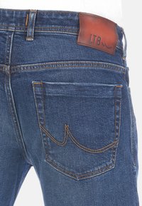 Jeans de mezclilla azul con costuras naranjas en contraste, un parche de cuero de LTB en la cinturilla y un diseño clásico de bolsillo.