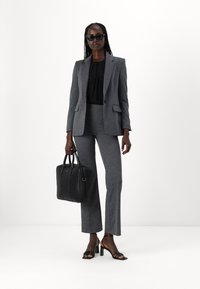 Gray tailored suit with fitted blazer and flared trousers. Black blouse underneath, black handbag, and strappy heels. Sunglasses included.