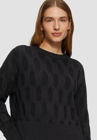 Maglione nero a maglia con un motivo testurizzato di aperture esagonali, colletto rotondo e polsini e orlo a coste.