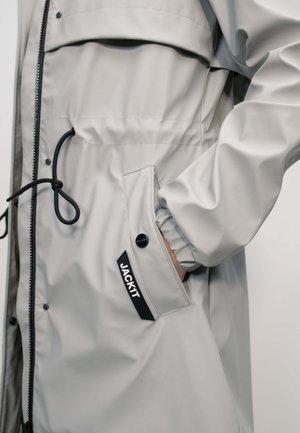 Light gray waterproof jacket with black drawstring, zipper, snap button pocket, and "JACK IT" label on the side.