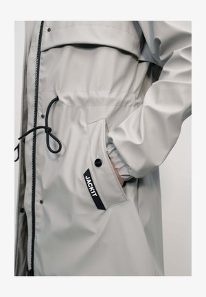 Light gray waterproof jacket with black drawstring, zipper, snap button pocket, and "JACK IT" label on the side.