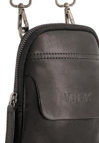 Sort lædertaske med lynlås, med tekstureret overflade og præget "VENEZIA" logo. Indeholder metalskær og en glat topkant.
