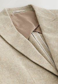 Beige strukturierter Blazer mit Reverskragen und einem glatten, hellbraunen Futter. Verfügt über einen Reißverschluss und ein dezentes Muster innen.