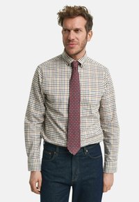 Rutet skjorte i creme, blå og rød med knap-ned krave; parret med et rødt slips med geometrisk mønster. Mørke jeans.