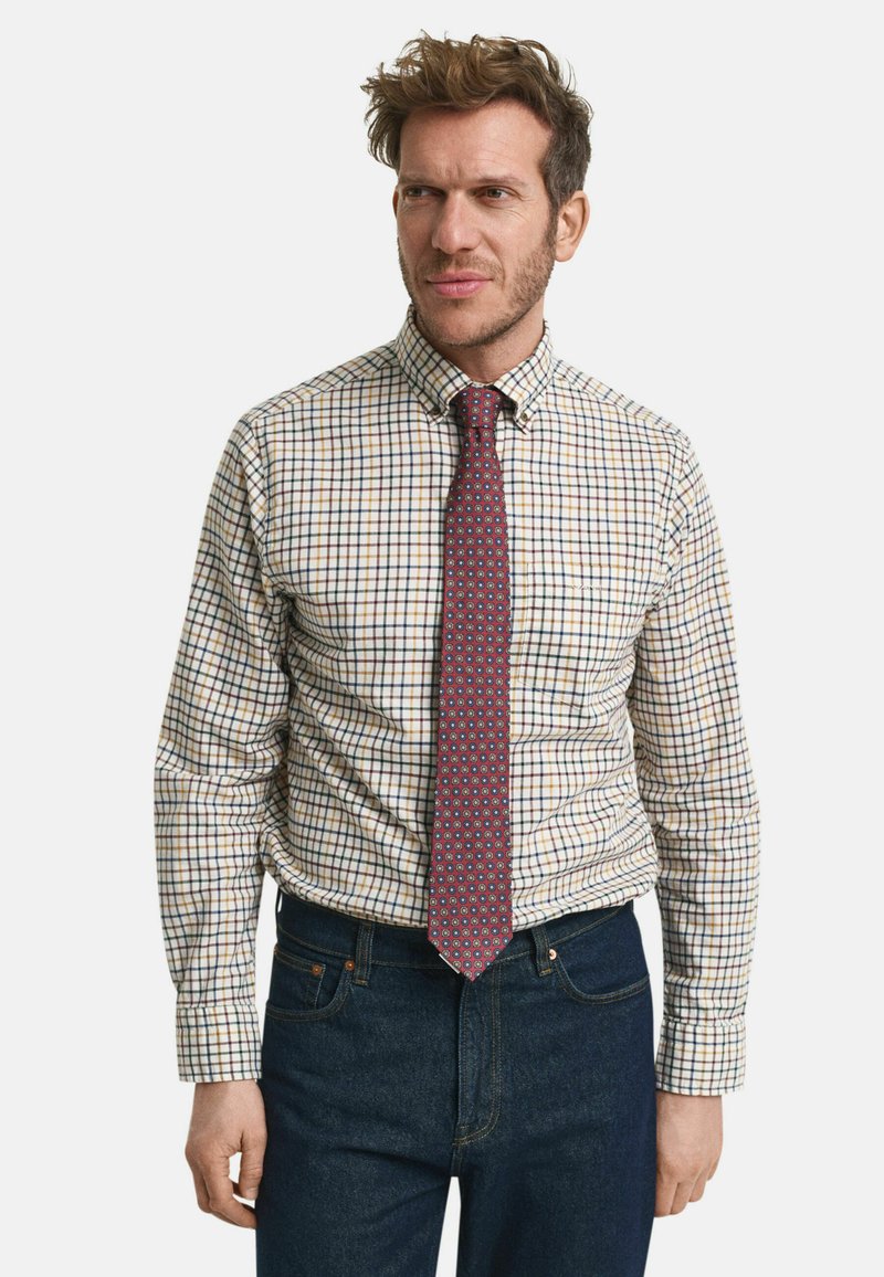 Rutet skjorte i creme, blå og rød med knap-ned krave; parret med et rødt slips med geometrisk mønster. Mørke jeans.
