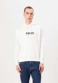 Hvid hætte sweatshirt med frontlomme, prydet med et sort logo i midten. Sammen med blå jeans, minimalisk design og blød tekstur.