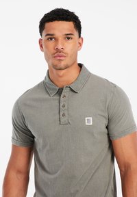 Korte mouw polo shirt in olijfgroen, met een knoopsluiting, kraag en een klein logopatch op de linkerkant van de borst. Katoenen stof.