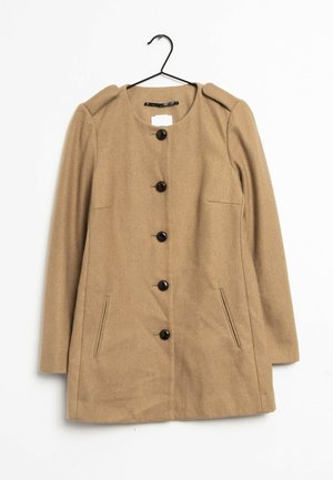 Manteau long beige à encolure ronde, boutons noirs sur le devant, deux poches latérales et épaulettes, suspendu à un cintre noir.