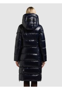 Polsterēts tumši zils parka ar augstu apkakli, spīdīgu virsmu un pārmērīga izmēra kapuci. Raksturots ar horizontālām šaurajām daļām un sānu rāvējslēdzēja kabatām.