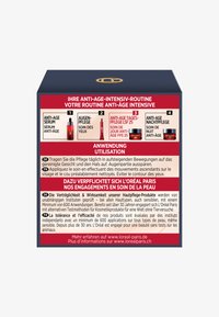 En kvadratisk, marinblå låda med en röd etikett och vit text som beskriver en anti-aging hudvårdsrutin; inkluderar grafiska bilder av produkter och instruktioner.