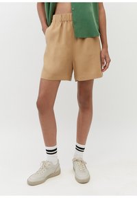 Beiga shorts med en elastisk midja, sidofickor och en avslappnad passform. I kombination med vita sneakers och mönstrade strumpor.