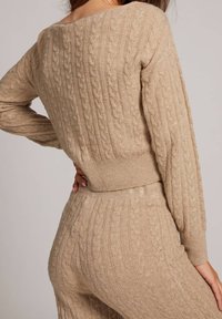 Completo beige a due pezzi in maglia con motivo a trecce, maniche lunghe e vita aderente. Tessuto morbido con dettagli a coste.